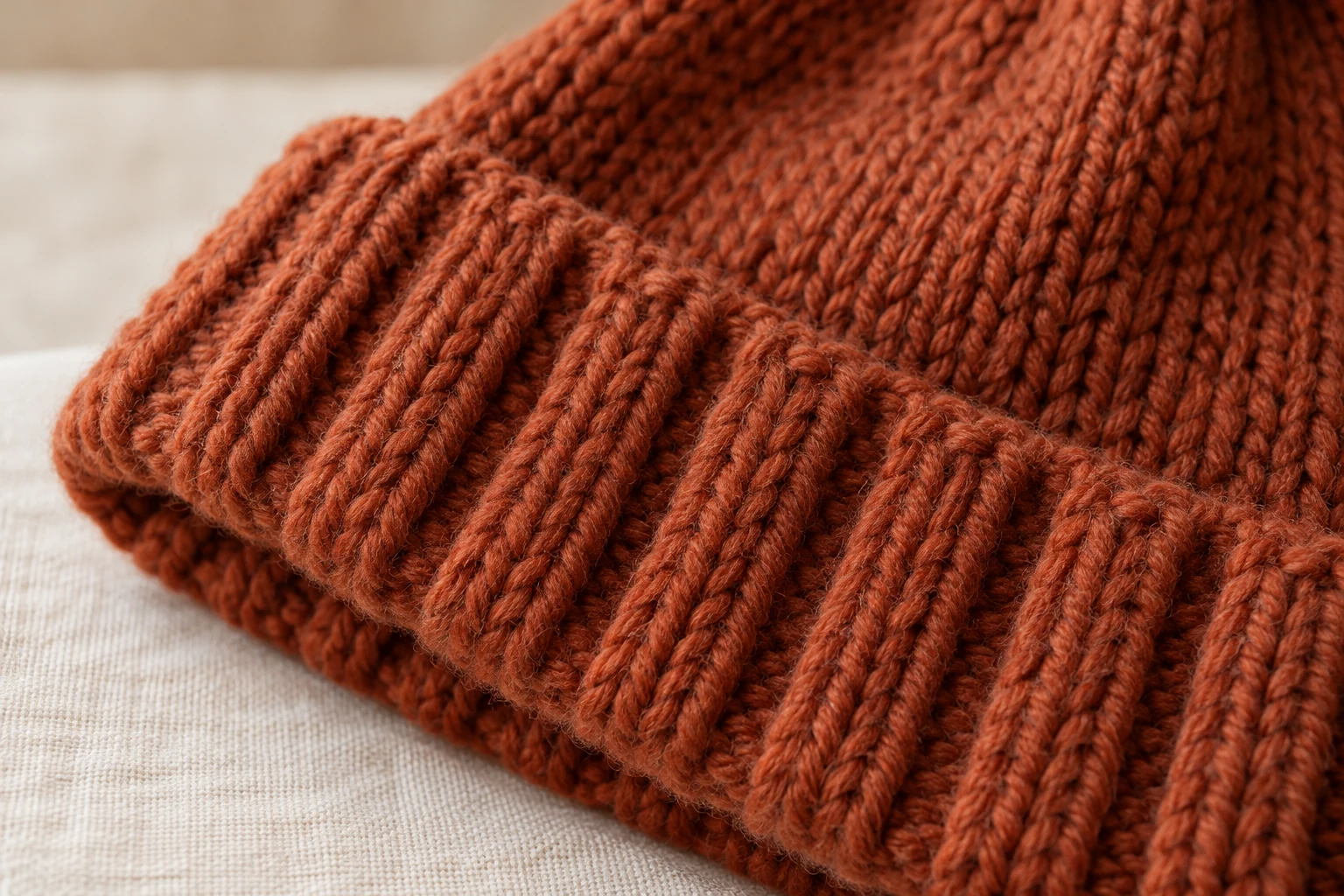 Close-up of the folded rib brim and stockinette fabric on a rust-orange chunky knit beanie